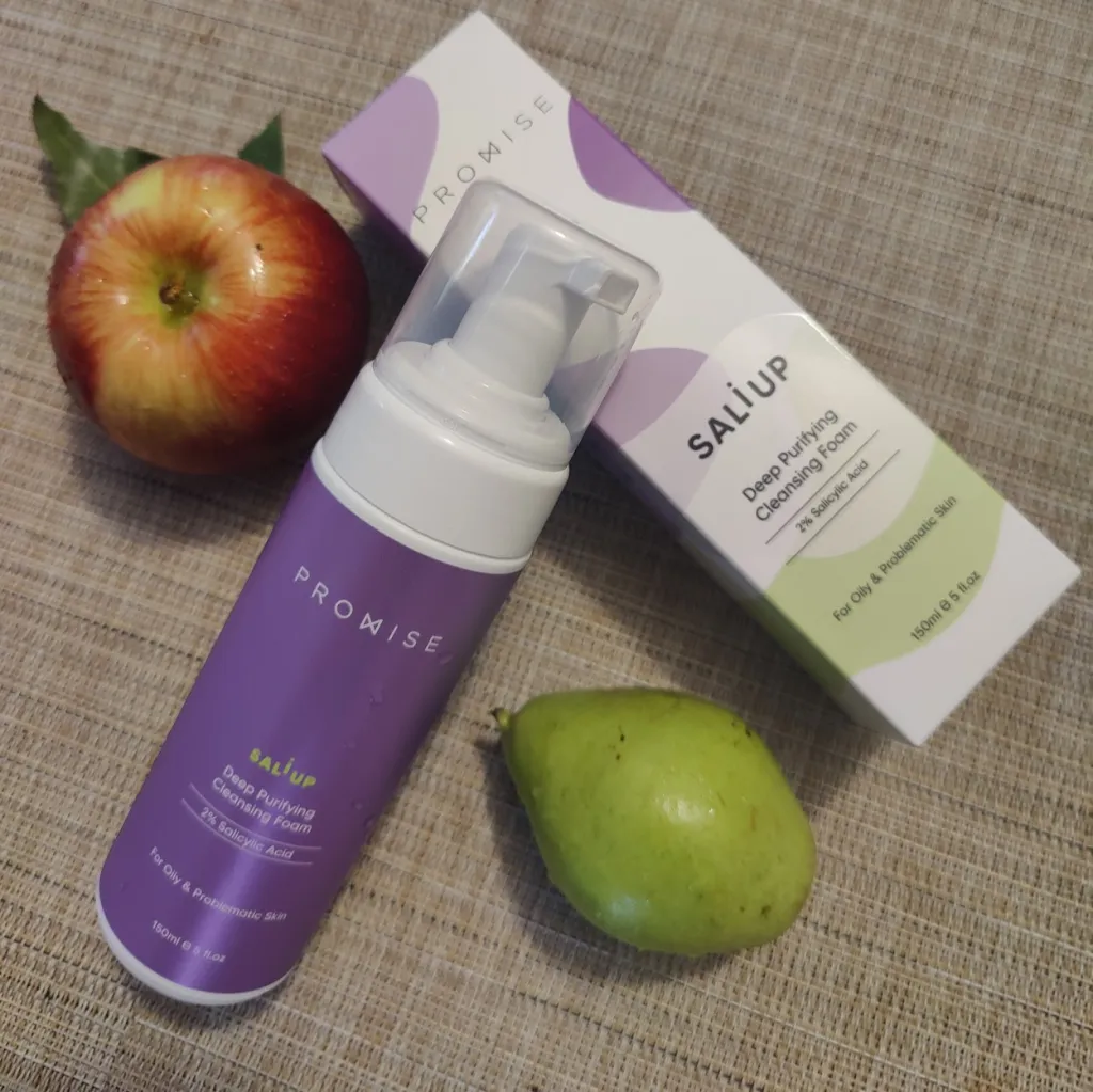 בקבוק קצץ ניקוי של מוצר בשם SaliUp ממוקם ליד תפוחים ואגסים על שולחן