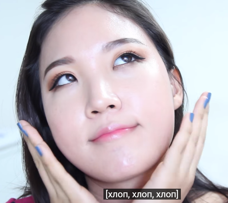 Young woman applying skincare product on her face with a gentle expression, showcasing a glowing complexion.
