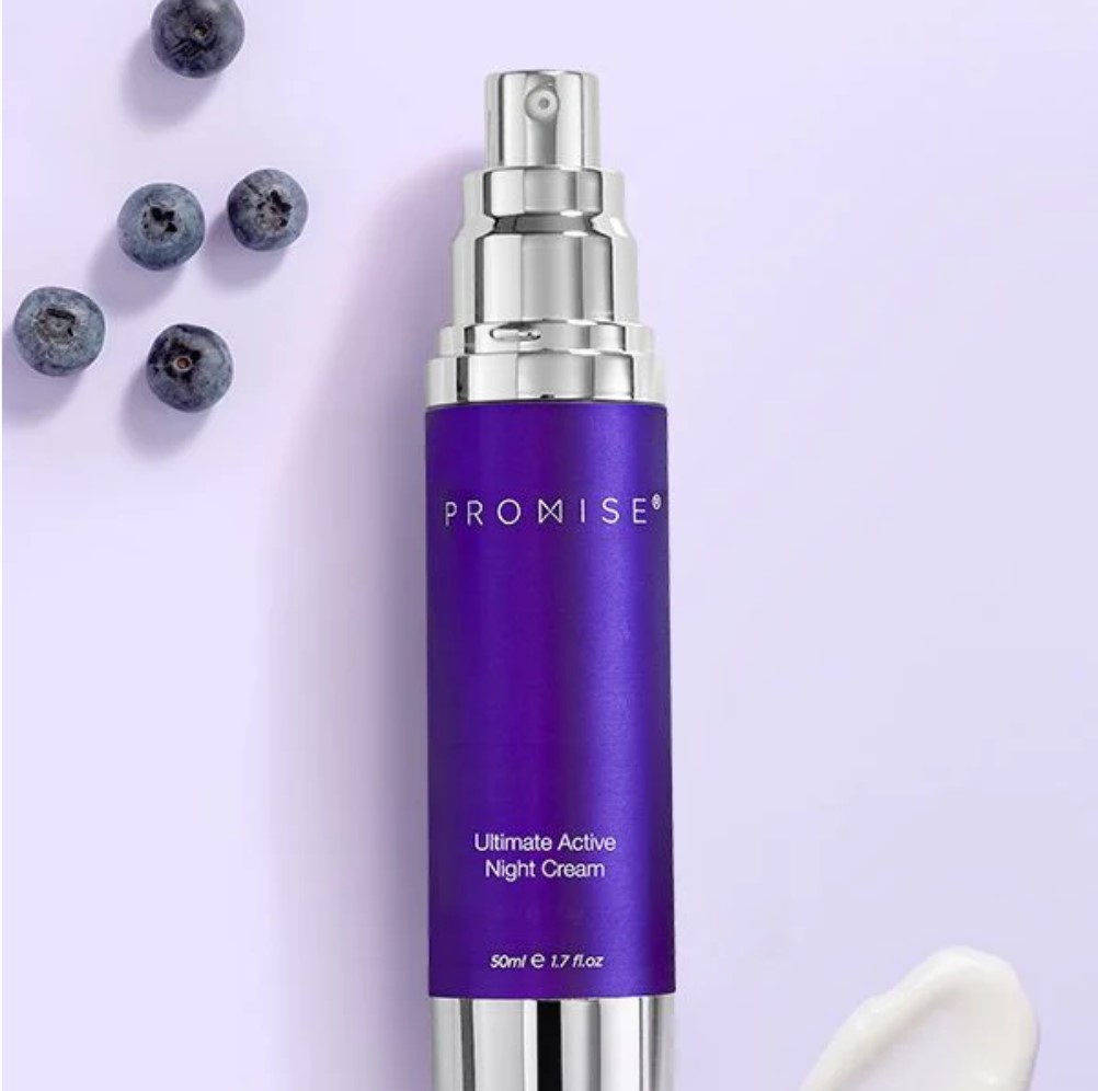 בקבוק של קרם לילה 'Ultimate Active Night Cream' של מותג PROMISE, בצבע סגול. ליד הבקבוק נמצאות כמה אוכמניות ומשחת קרם לבנה.
