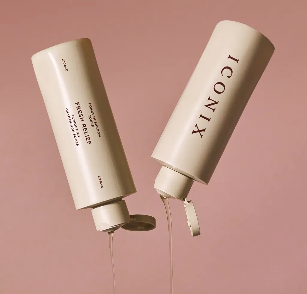 שני בקבוקי טונר ICONIX באלמנט עיצוב מינימליסטי, המפיצים נוזל דמוי טונר על רקע ורוד.