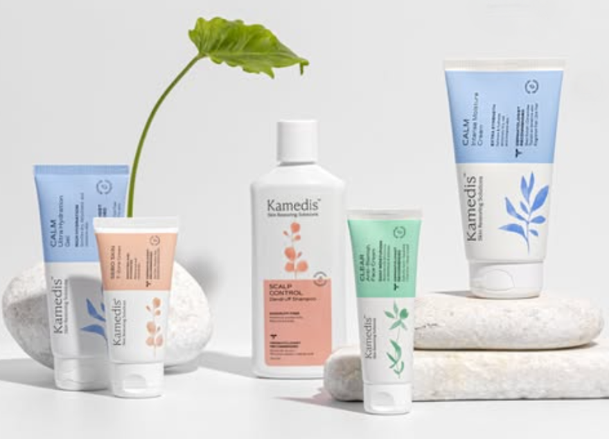 מגוון מוצרי שיער ועור של קמדיס, כולל טיפולי עור היפואלרגניים, מונחים על רקע לבן עם צמח ירוק ואבנים לבנות.