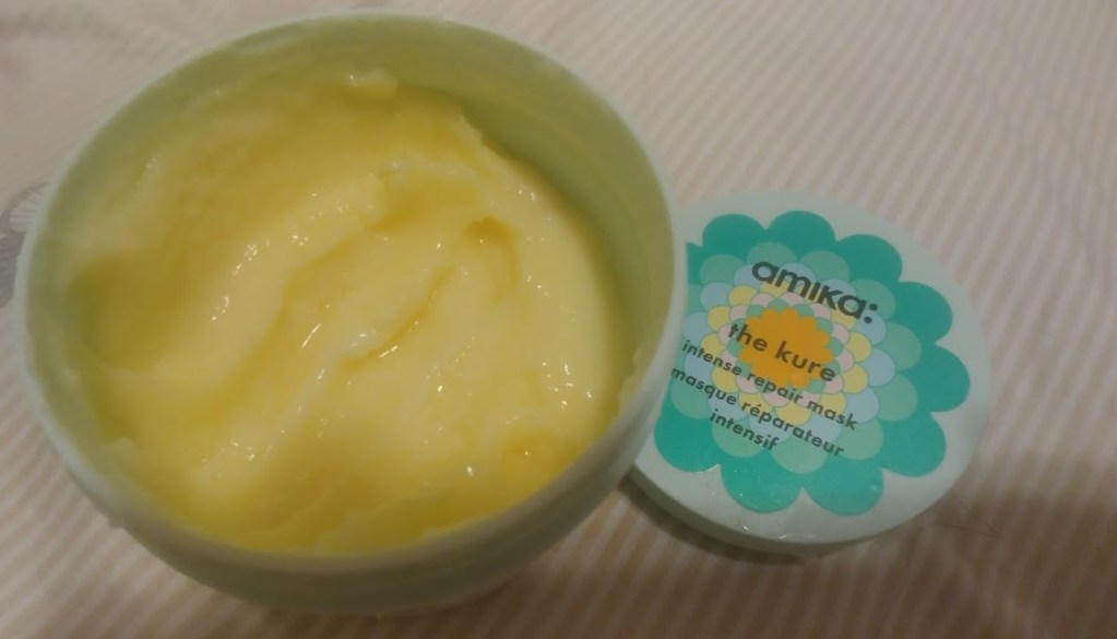 קופסה פתוחה עם מסיכת שיער של Amika, צבעה צהוב והמרקם קרם.