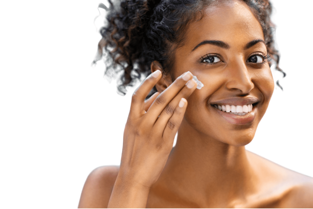 אישה עם שיער מתולתל, מחייכת ומספיגה קרם על פניה.