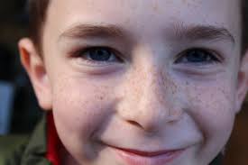 Close-up of a smiling child's face with freckles and blue eyes.