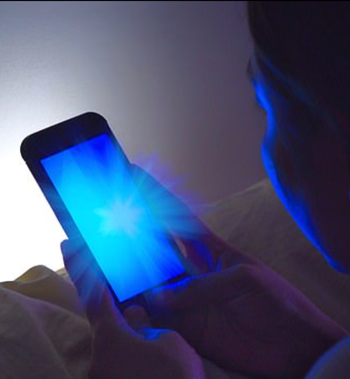 אדם בעמדה בינונית מחזיק בטלפון סלולרי המואר באור כחול חזק, במצב חשוך.